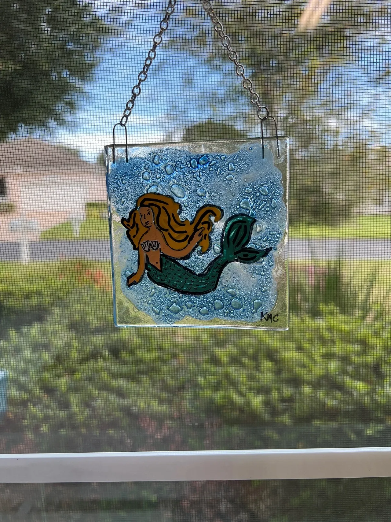 Hanging mermaid art against outdoor scenery.